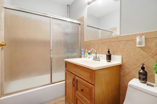 bathroom featuring tile walls, toilet, vanity, shower / bath combination with glass door, and backsplash