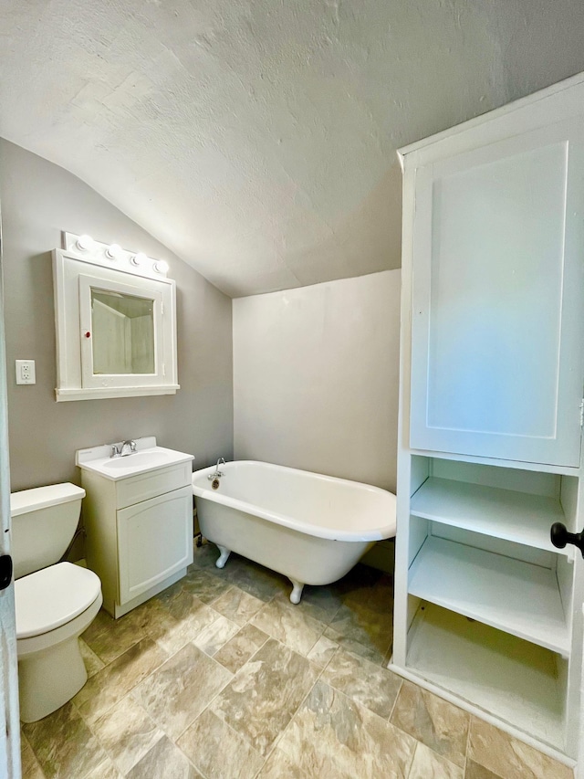 full bathroom with lofted ceiling, toilet, a freestanding tub, vanity, and stone finish floors