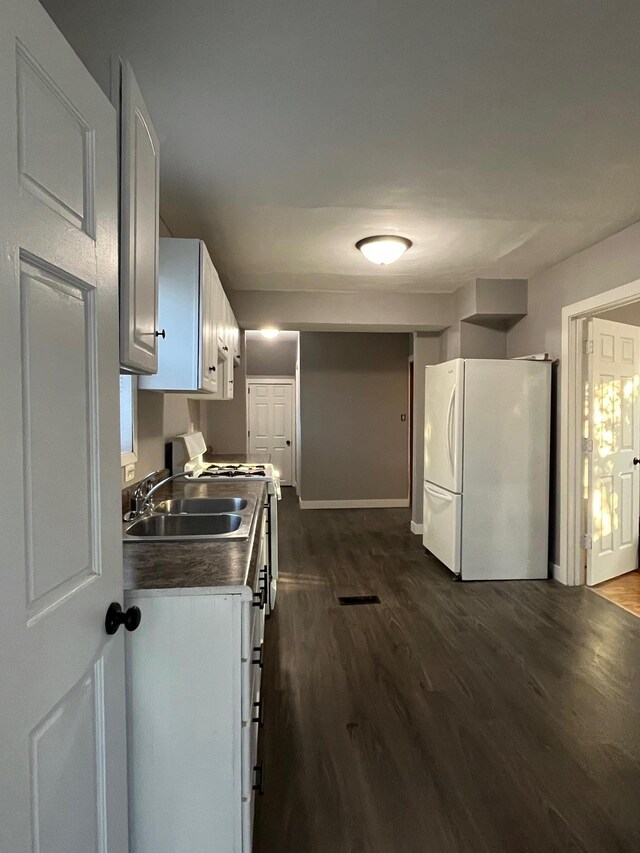 kitchen with freestanding refrigerator, a sink, dark wood-type flooring, white cabinetry, and baseboards
