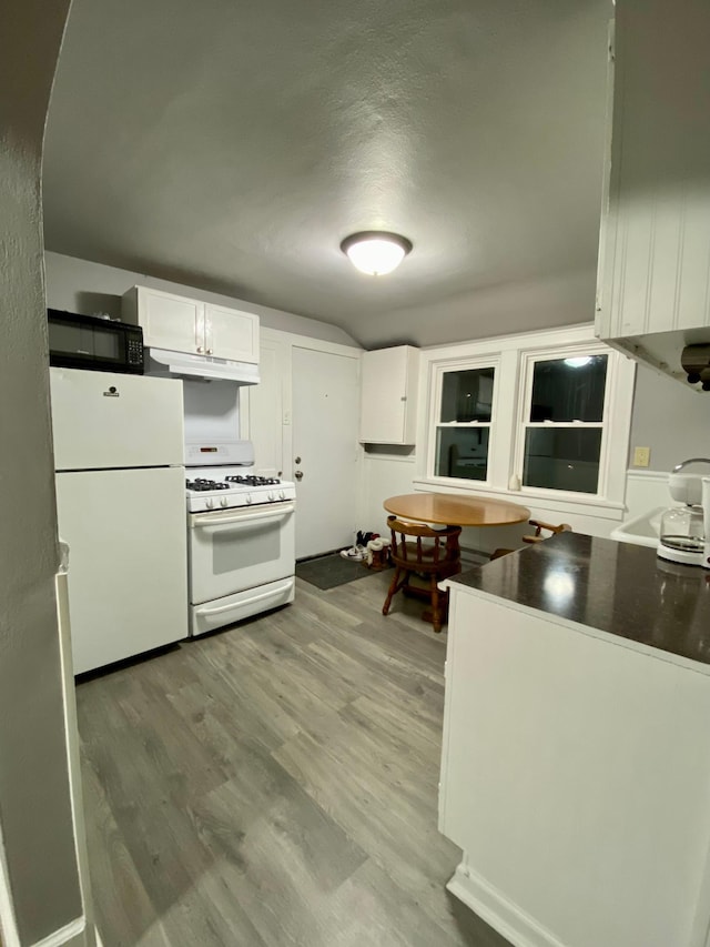 kitchen featuring white appliances, white cabinets, light wood finished floors, under cabinet range hood, and dark countertops