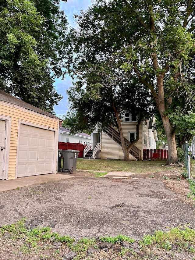 view of yard with an outbuilding, a garage, fence, dirt driveway, and stairway
