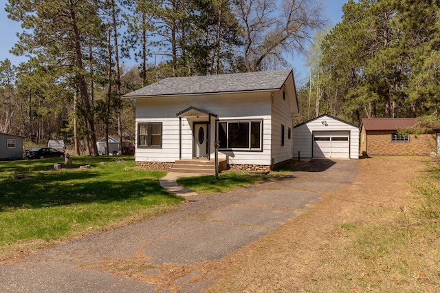 bungalow featuring asphalt driveway, an outbuilding, a detached garage, a front lawn, and a shingled roof