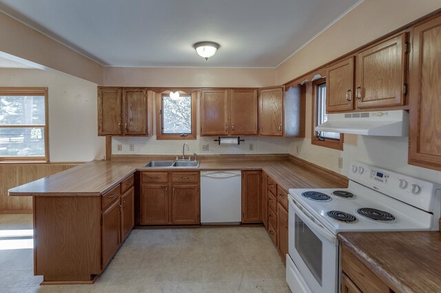 kitchen with white appliances, a peninsula, under cabinet range hood, a sink, and brown cabinets