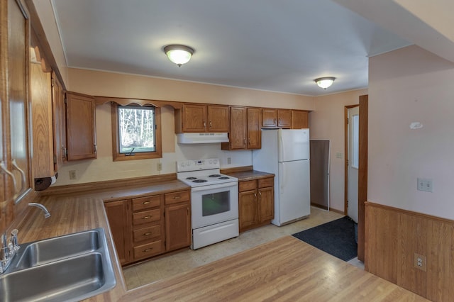 kitchen featuring white appliances, a sink, under cabinet range hood, brown cabinetry, and light countertops