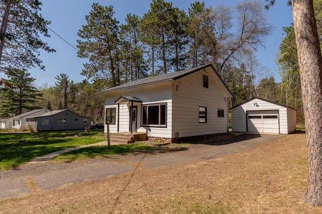 view of front facade with a detached garage, an outdoor structure, asphalt driveway, and a front lawn