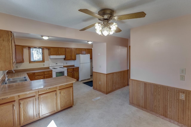 kitchen with white appliances, a sink, a wainscoted wall, a ceiling fan, and under cabinet range hood