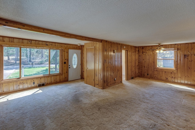 unfurnished living room featuring a textured ceiling, wooden walls, and carpet flooring