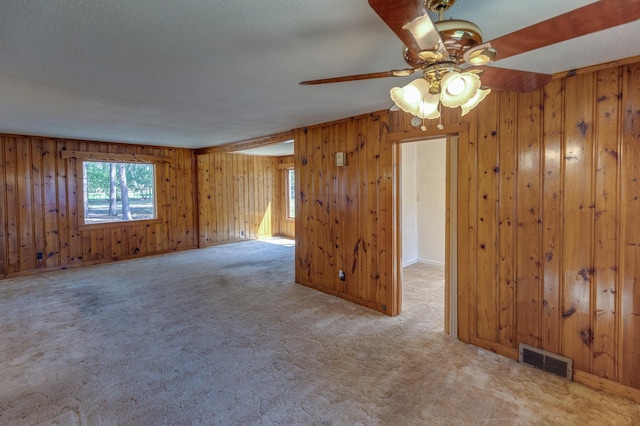 carpeted empty room featuring a ceiling fan, wood walls, and a textured ceiling