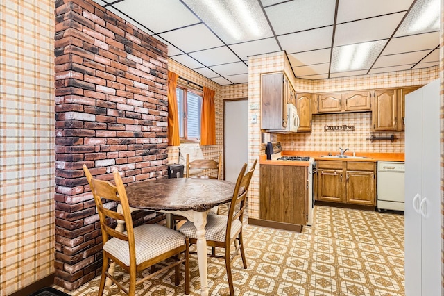 dining area featuring a drop ceiling, light flooring, and brick wall