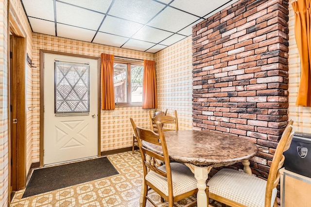 dining area with a paneled ceiling, wallpapered walls, tile patterned floors, and baseboards