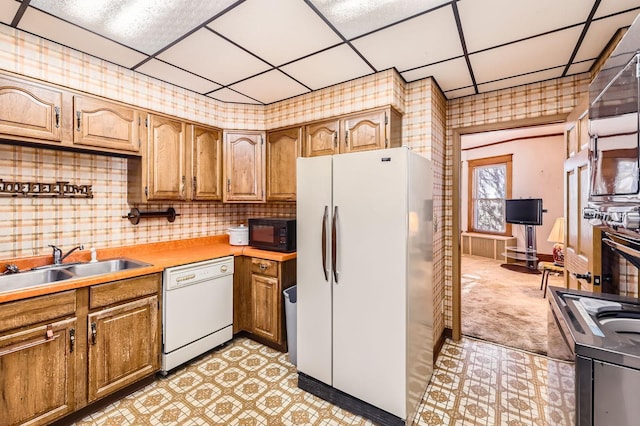 kitchen featuring white appliances, a sink, a drop ceiling, brown cabinetry, and light countertops