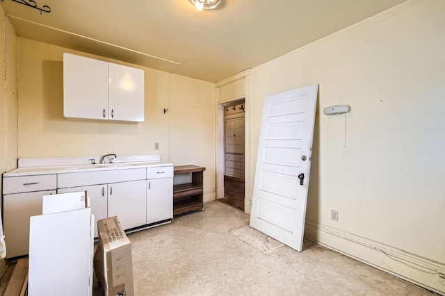 kitchen featuring a sink, light countertops, concrete flooring, and white cabinets