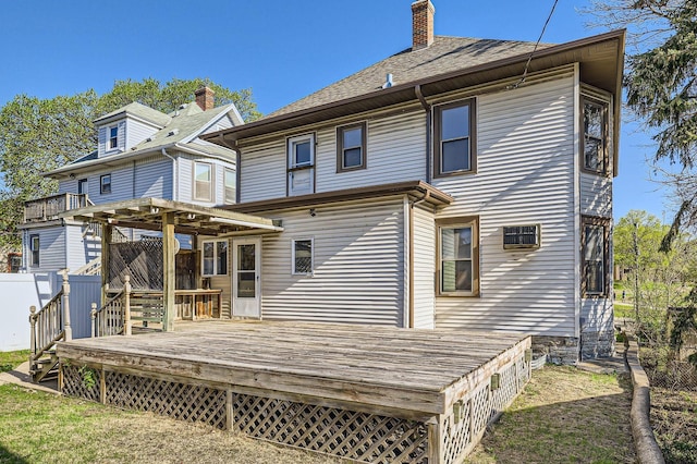 rear view of property featuring a deck, a chimney, and roof with shingles