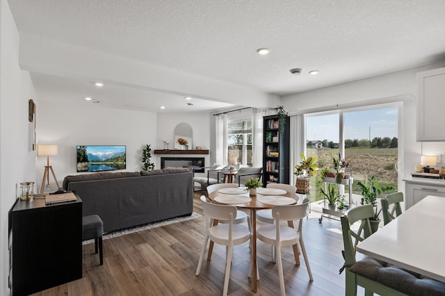 dining area featuring wood finished floors, a textured ceiling, recessed lighting, and a glass covered fireplace