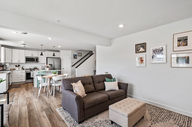 living room featuring light wood-style floors, recessed lighting, baseboards, and stairs