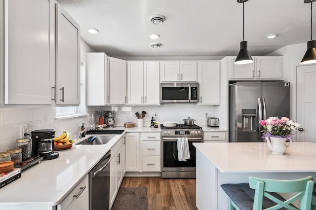 kitchen featuring stainless steel appliances, a sink, light countertops, a textured ceiling, and dark wood-style flooring