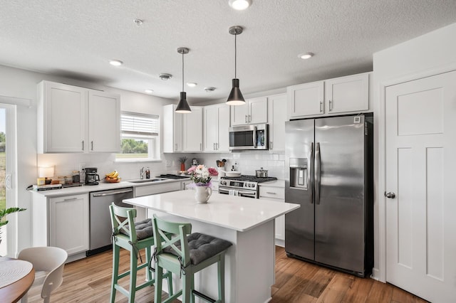 kitchen with stainless steel appliances, tasteful backsplash, wood finished floors, light countertops, and a textured ceiling