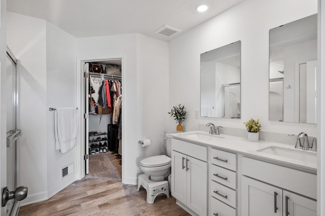 bathroom with wood finished floors, double vanity, a spacious closet, toilet, and recessed lighting