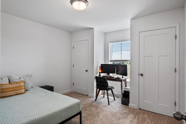 bedroom featuring light carpet, a desk, baseboards, and a textured ceiling