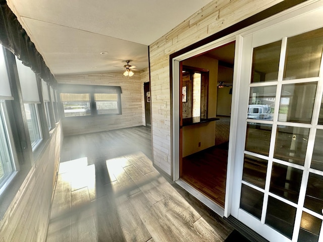 hallway featuring wood walls, wood finished floors, and lofted ceiling
