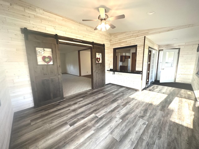 unfurnished room featuring a barn door, ceiling fan, wood finished floors, and wooden walls