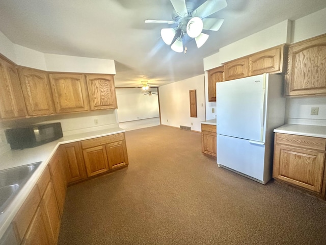 kitchen featuring freestanding refrigerator, a ceiling fan, dark colored carpet, and light countertops