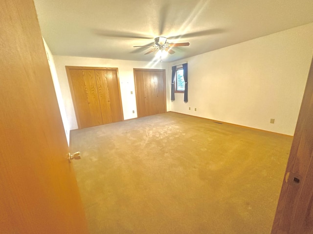 unfurnished bedroom with two closets, carpet floors, and a ceiling fan