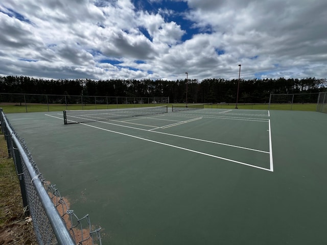 view of tennis court with community basketball court, fence, and a forest view