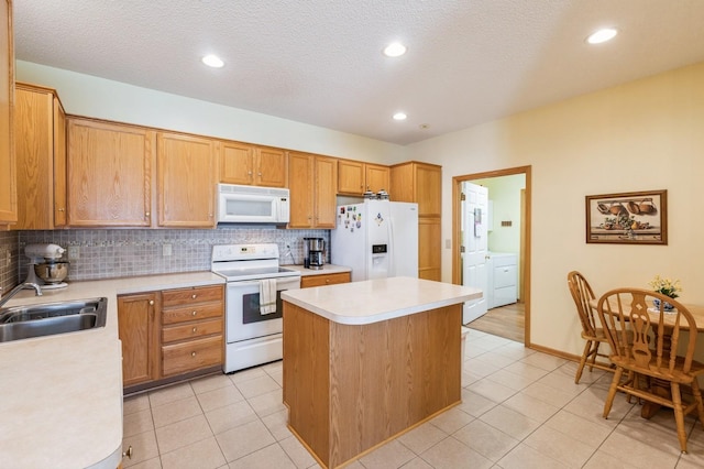 kitchen featuring white appliances, a sink, washer and clothes dryer, light countertops, and a center island