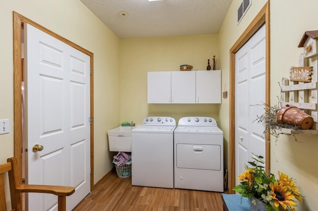 washroom featuring cabinet space, separate washer and dryer, light wood-type flooring, a textured ceiling, and baseboards