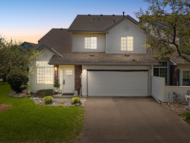 traditional-style home featuring an attached garage, roof with shingles, driveway, a front lawn, and brick siding