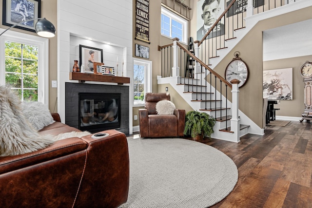 living area featuring a brick fireplace, plenty of natural light, stairway, and a high ceiling