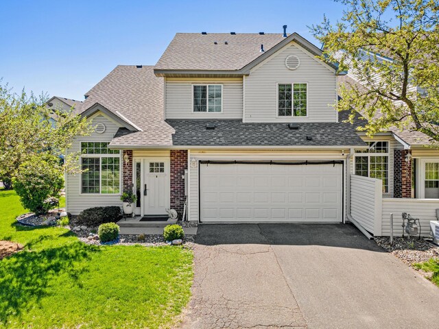 traditional-style home featuring driveway, a garage, a shingled roof, a front yard, and brick siding
