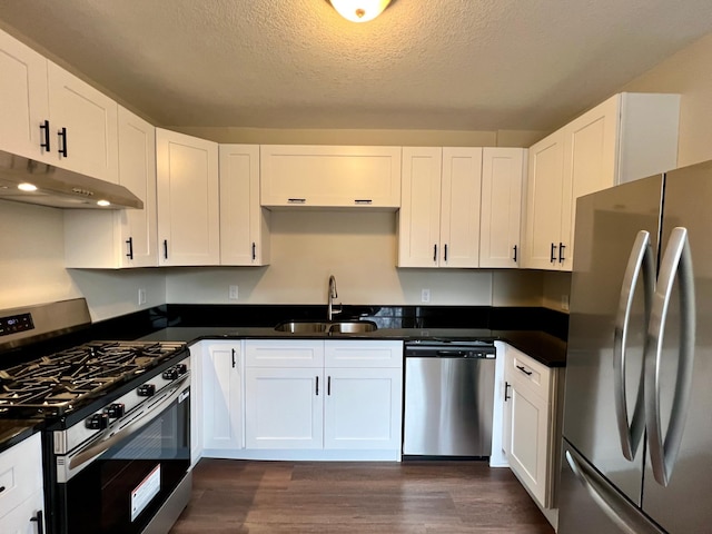 kitchen with stainless steel appliances, a sink, under cabinet range hood, dark wood-style flooring, and dark countertops