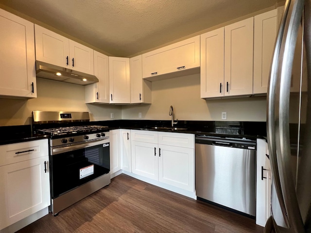 kitchen with appliances with stainless steel finishes, a sink, under cabinet range hood, dark wood finished floors, and white cabinets