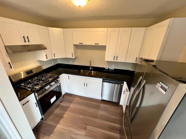 kitchen featuring stainless steel appliances, under cabinet range hood, a sink, dark wood-type flooring, and white cabinets