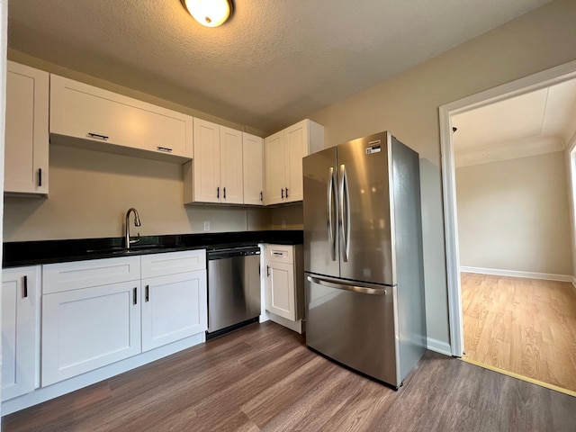 kitchen with appliances with stainless steel finishes, a sink, dark wood finished floors, dark countertops, and a textured ceiling