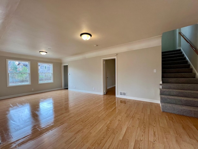 unfurnished living room with stairway, light wood finished floors, and baseboards