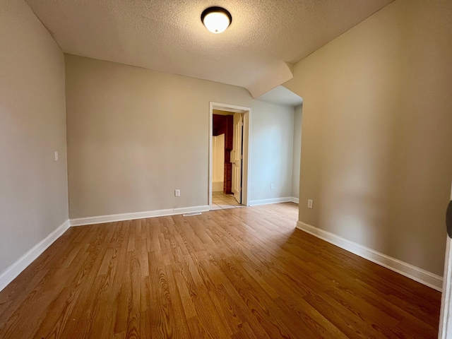 empty room featuring wood finished floors, a textured ceiling, and baseboards