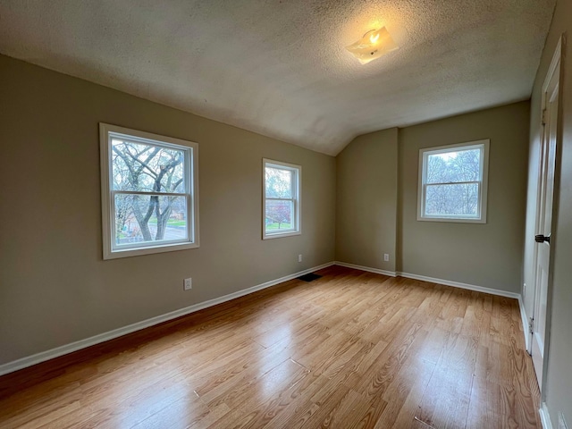 unfurnished bedroom with wood finished floors, vaulted ceiling, multiple windows, baseboards, and a textured ceiling
