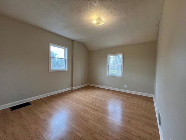 empty room with healthy amount of natural light, vaulted ceiling, wood finished floors, baseboards, and a textured ceiling