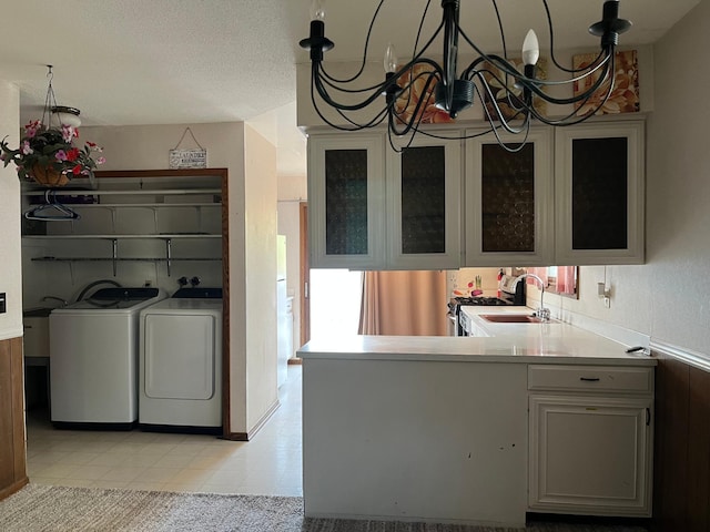 kitchen featuring washing machine and clothes dryer, a sink, a chandelier, glass insert cabinets, and light countertops