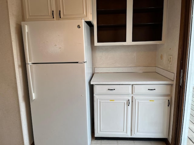 kitchen with freestanding refrigerator, light countertops, open shelves, and white cabinetry
