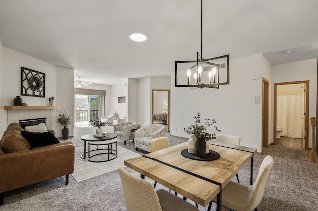 dining room with a tiled fireplace, light colored carpet, a chandelier, ceiling fan, and a textured ceiling