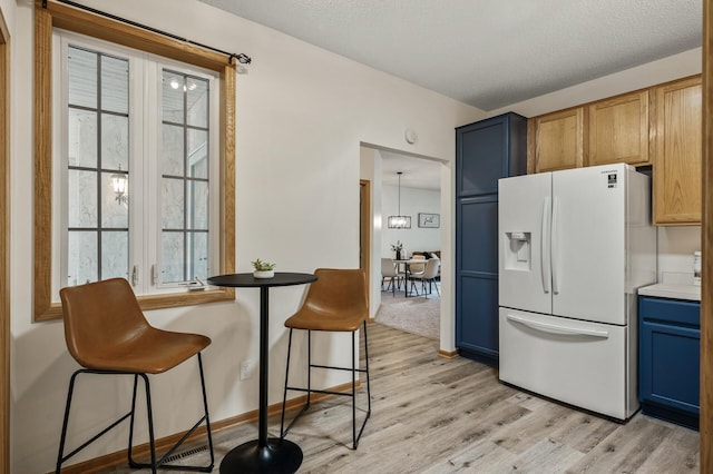 kitchen with white fridge with ice dispenser, light wood-style flooring, blue cabinetry, a kitchen breakfast bar, and light countertops