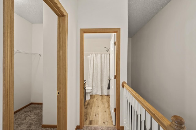 corridor with a textured ceiling, an upstairs landing, and baseboards