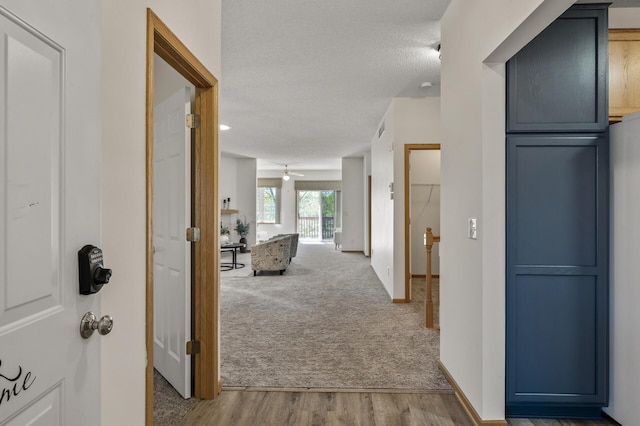 corridor with carpet flooring, wood finished floors, and a textured ceiling