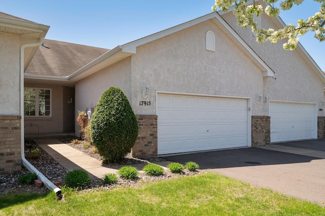 view of home's exterior featuring brick siding, an attached garage, asphalt driveway, and stucco siding