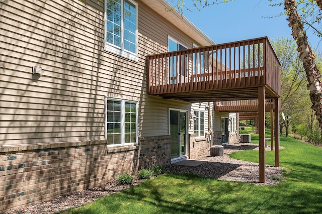 rear view of house featuring a deck, a lawn, brick siding, and central air condition unit