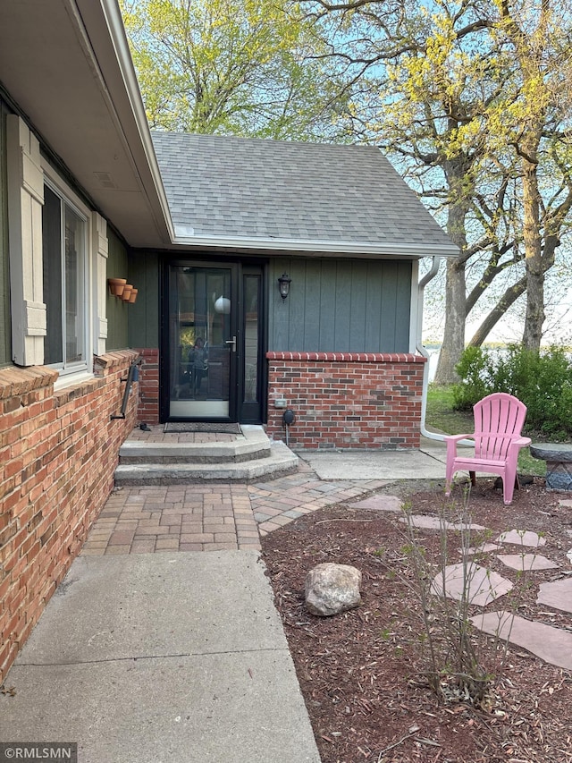 view of exterior entry with brick siding and a shingled roof